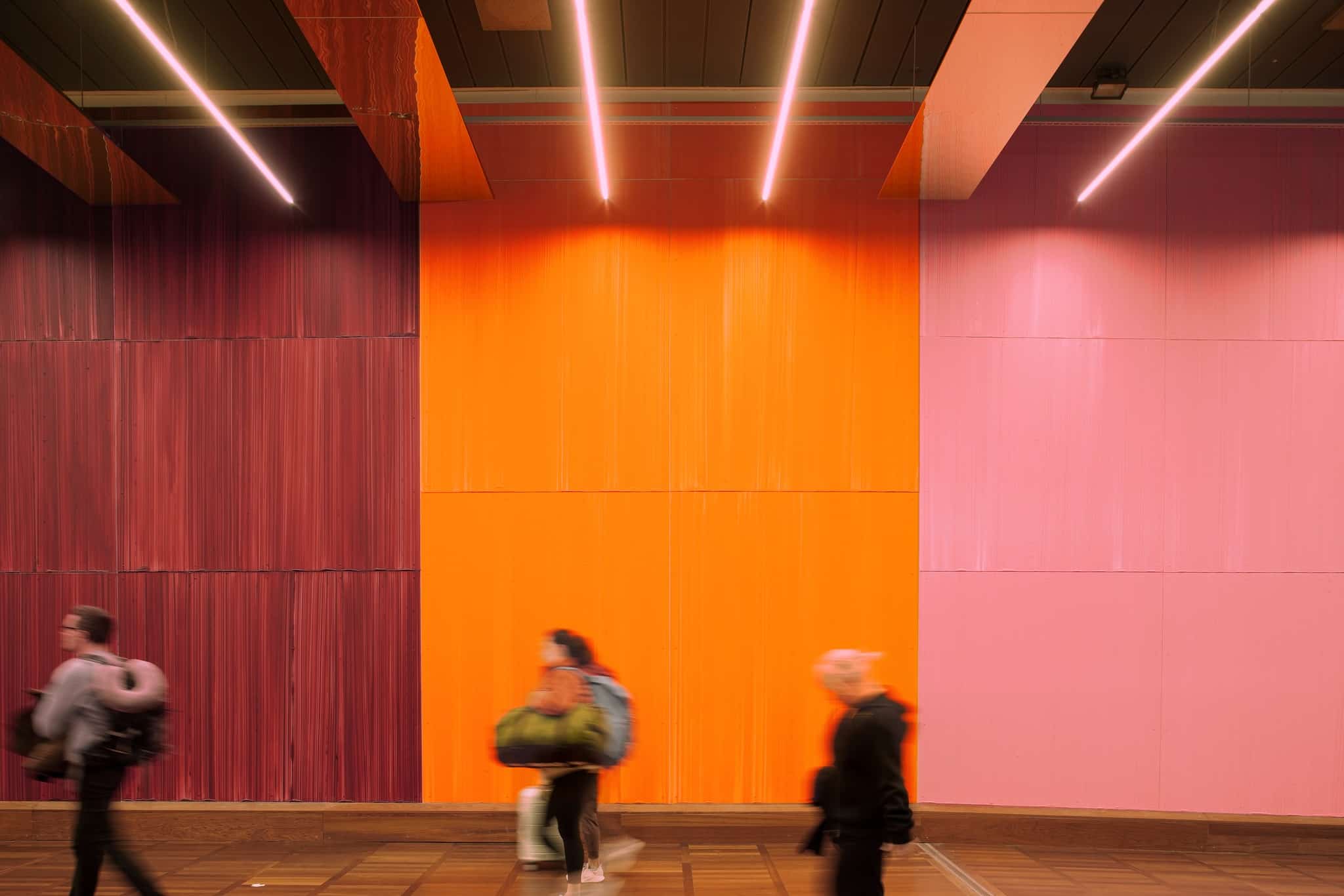 Københavns Lufthavn - Zeso Architects - www.zeso.dk - Farverig baggrund, vinrød, orange og rosa væg, med loftsbelysning og folk der går forbi
