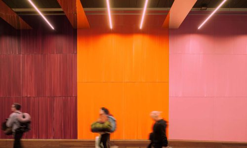 Københavns Lufthavn - Zeso Architects - www.zeso.dk - Farverig baggrund, vinrød, orange og rosa væg, med loftsbelysning og folk der går forbi
